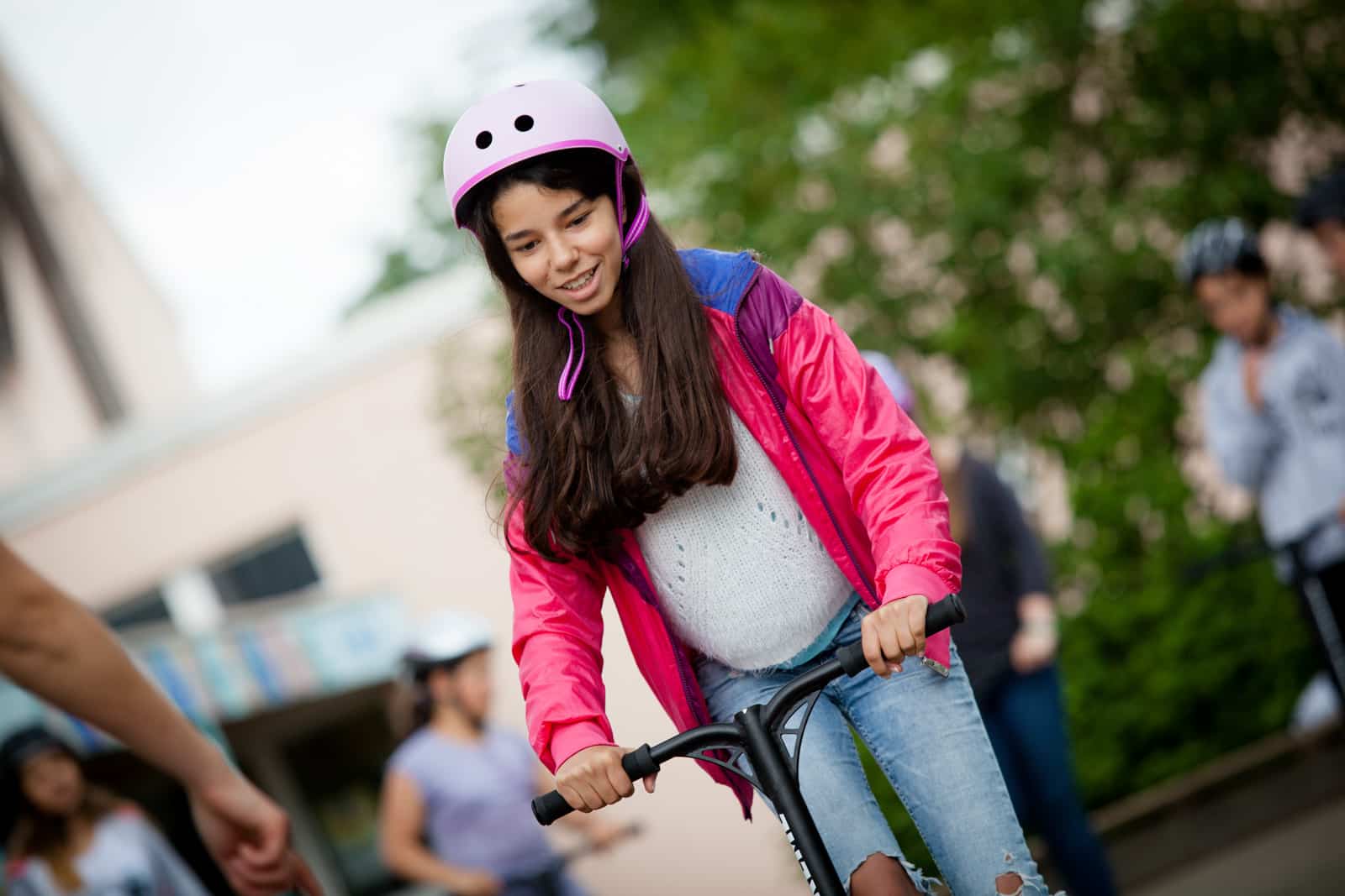 Ein Mädchen mit rosa Helm fährt Scooter