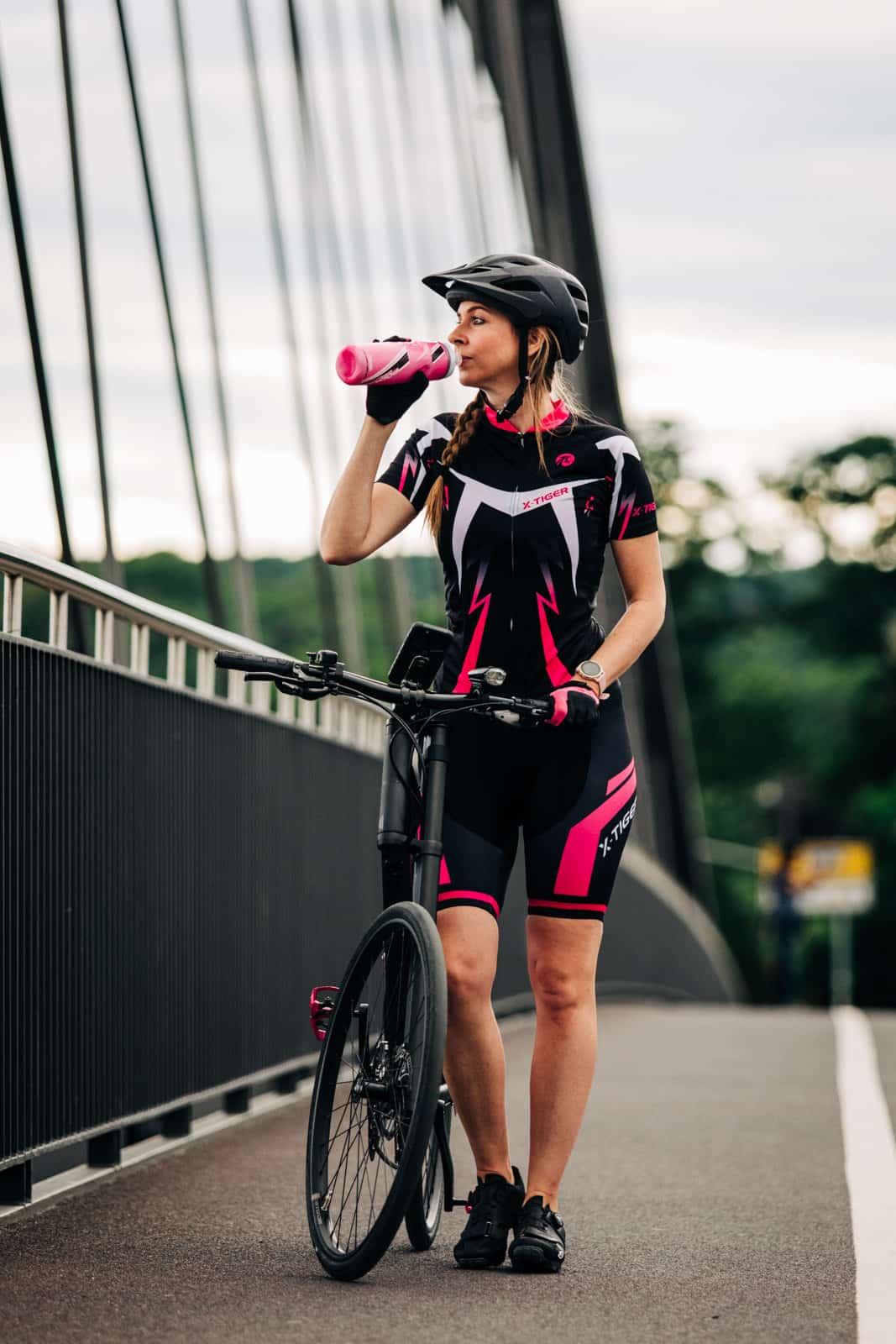 Frau trinkt aus Trinkflasche und schiebt dabei ihr Fahrrad